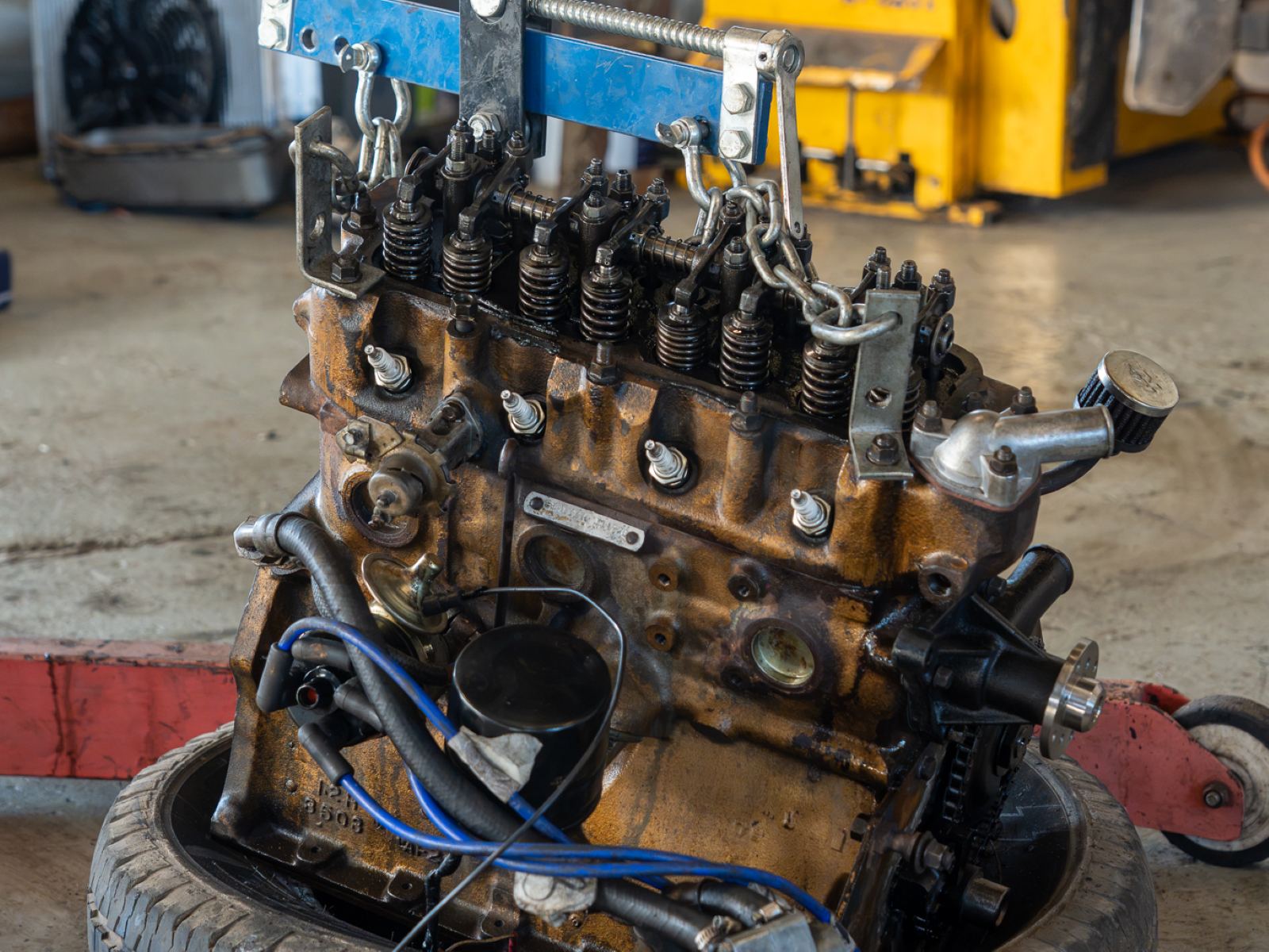 An engine lifted out of a car and hanging from the workshop crane
