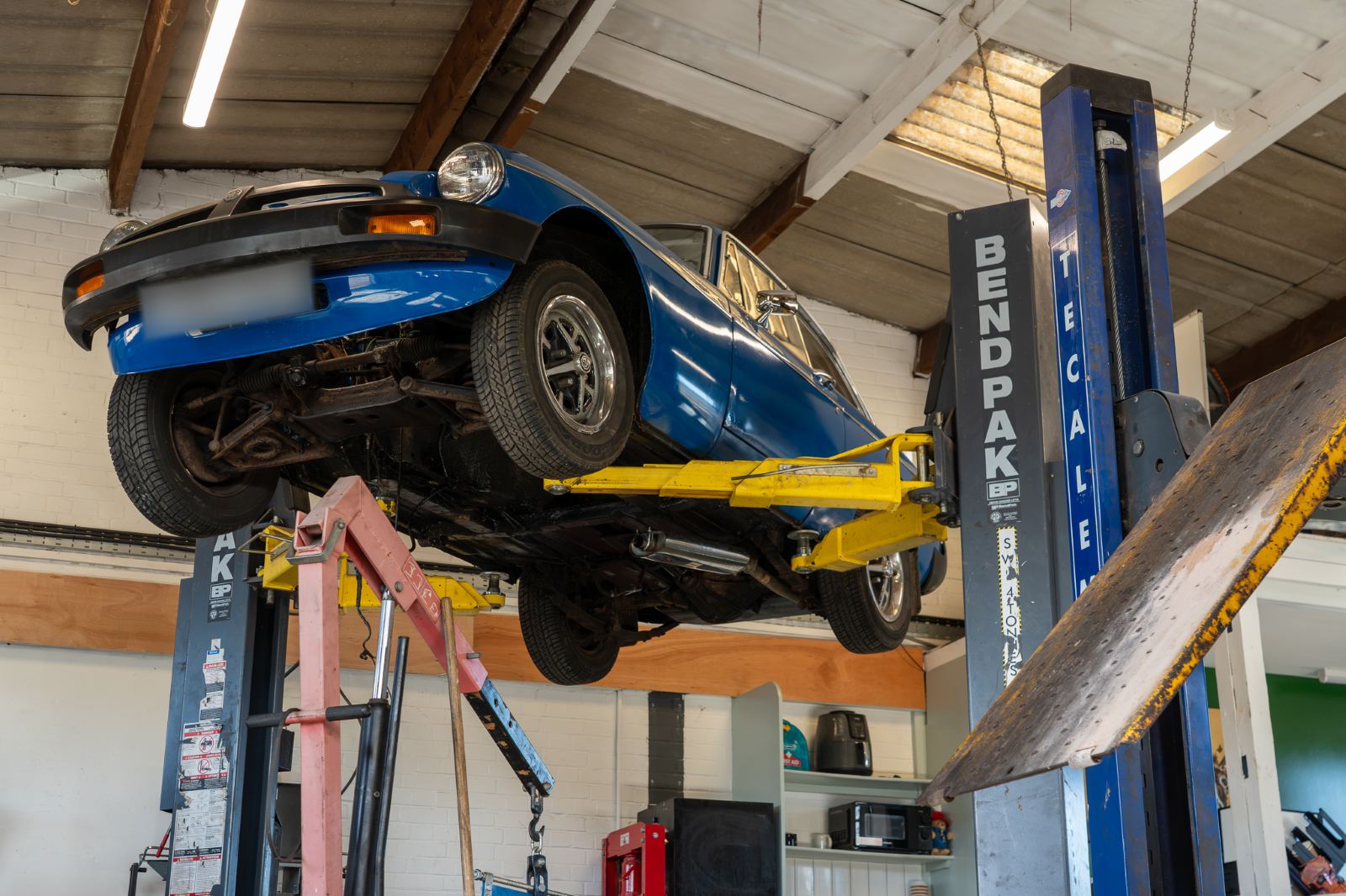 A blue MG raised on a two-post lift in the workshop