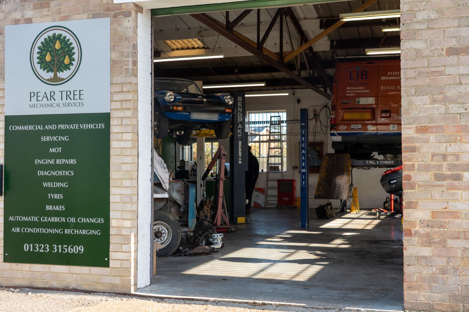 The Pear Tree Mechanical Services sign beside the workshop door, listing servicing, MOT, engine repairs, diagnostics, welding, tyres, brakes, gearbox oil changes and air conditioning